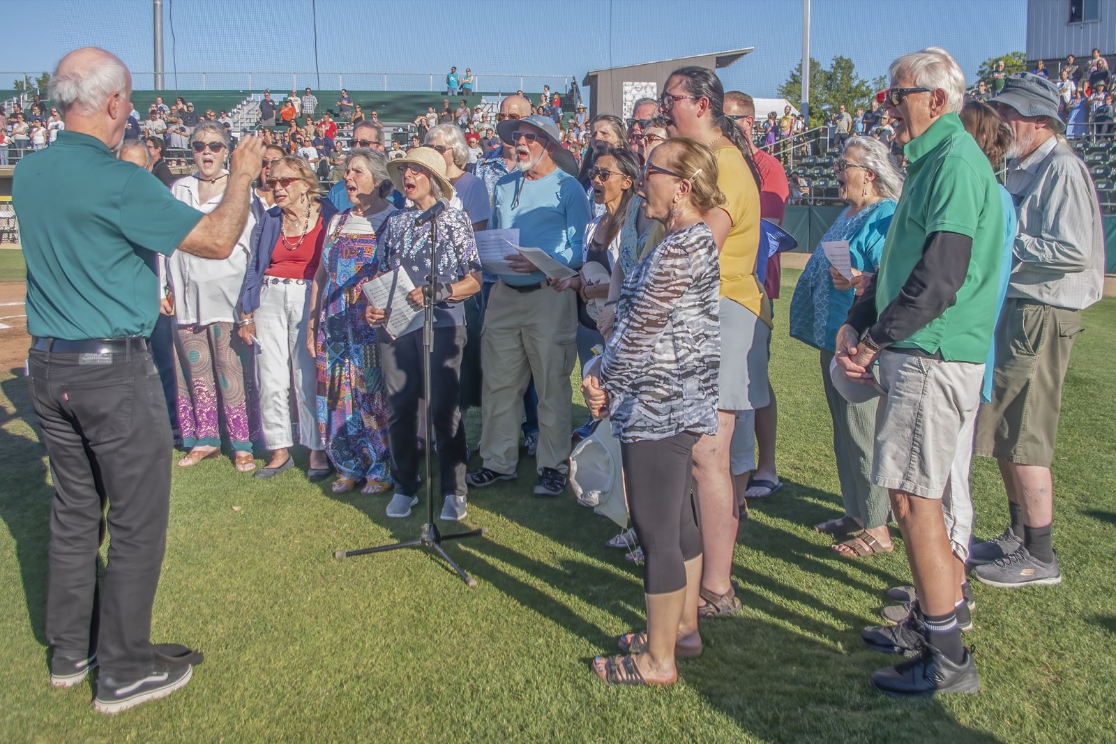 Wide view of the choir on the field with the crowd standing in the bleachers